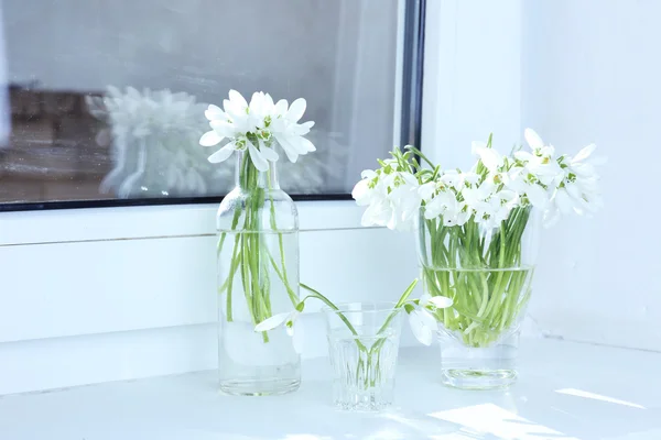 Beautiful bouquets of snowdrops in vases on windowsill — Stock Photo, Image