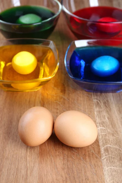 Cuencos con pintura para huevos de Pascua y huevos sobre mesa de madera —  Fotos de Stock