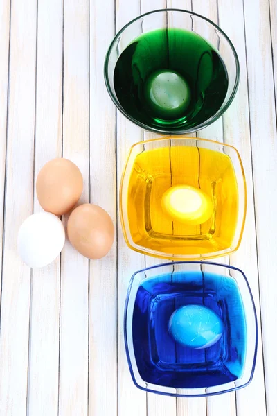 Bowls with paint for Easter eggs and eggs on wooden table — Stock Photo, Image
