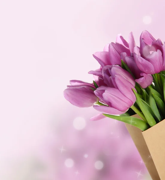 Beautiful bouquet of purple tulips in paper bag on bright background — Stock Photo, Image