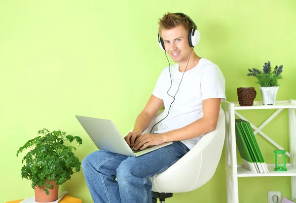 Молодой человек расслабляется с ноутбуком в кресле, на домашнем фоне интерьера — стоковое фото