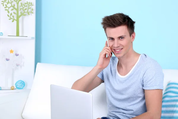 Mann spricht von Telefon mit Laptop auf blauem Hintergrund — Stockfoto