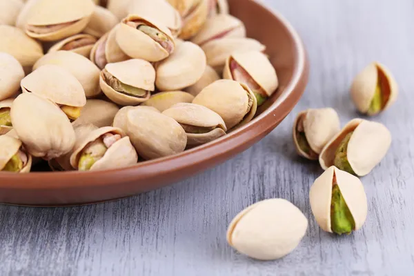 Pistachio nuts on plate on wooden background — Stock Photo, Image