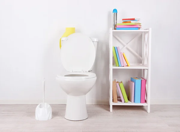 Weiße Toilettenschüssel und Ständer mit Büchern, auf farbigem Wandhintergrund — Stockfoto