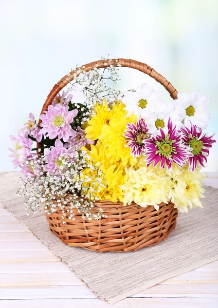 Beautiful chrysanthemum flowers in wicker basket on table on light background