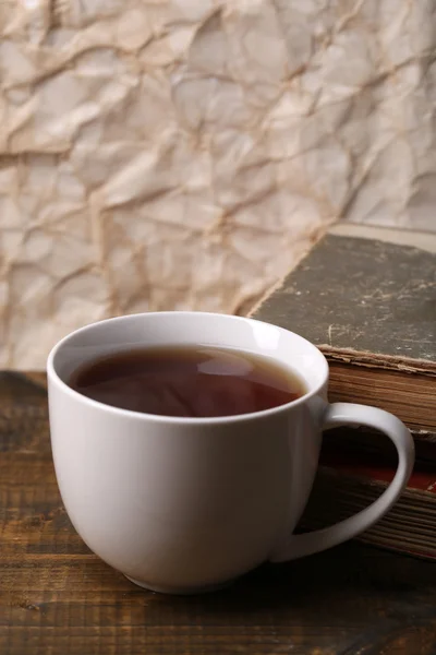 Kopp varm te med böcker på bord på papper bakgrund — Stockfoto