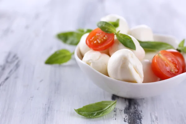 Tasty mozzarella cheese with basil and tomatoes in bowl, on wooden table — Stock Photo, Image