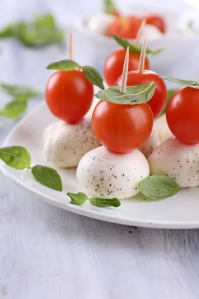 Schmackhafter Mozzarella-Käse mit Basilikum und Tomaten auf Teller, auf Holztisch — Stockfoto