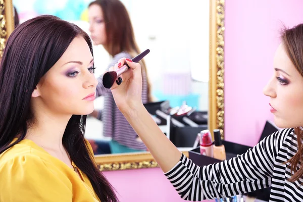 Mujer joven estilista haciendo maquillaje hermosa chica en salón de belleza — Foto de Stock