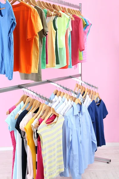 Different clothes on hangers, on pink background — Stock Photo, Image