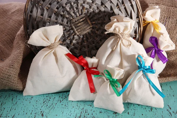 Sacks on color wooden table, on sackcloth background — Stock Photo, Image