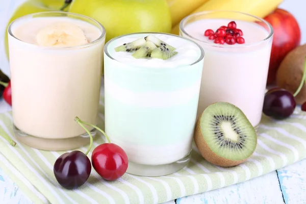 Delicioso yogur con sabores de frutas en vasos y frutas frescas en servilleta, sobre fondo claro —  Fotos de Stock