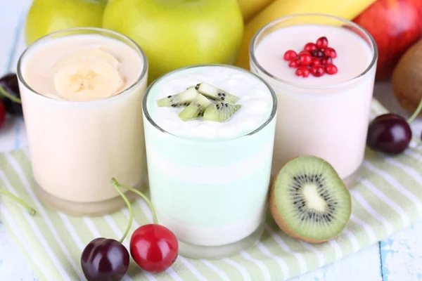 Délicieux yaourt aux fruits goûts dans les verres et les fruits frais sur la serviette, sur fond clair — Photo