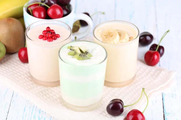 Délicieux yaourt aux fruits goûts dans les verres et les fruits frais sur la serviette, sur fond de bois couleur — Photo