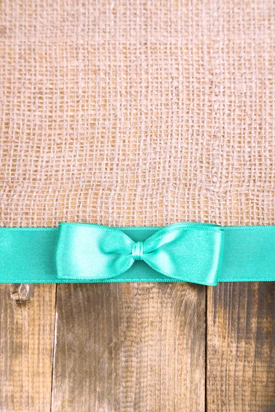 Sackcloth with color ribbon and bow on wooden background — Stock Photo, Image