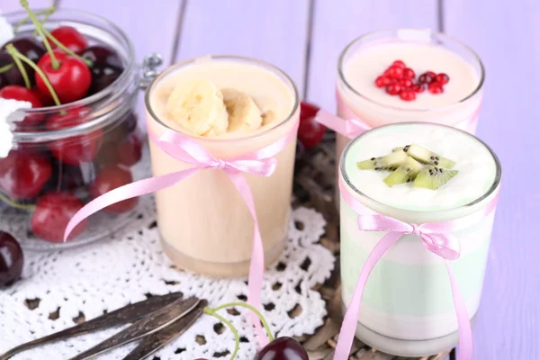 Finom joghurt gyümölcs íze, szemüveg és friss gyümölcsök színes fából készült háttér — Stock Fotó