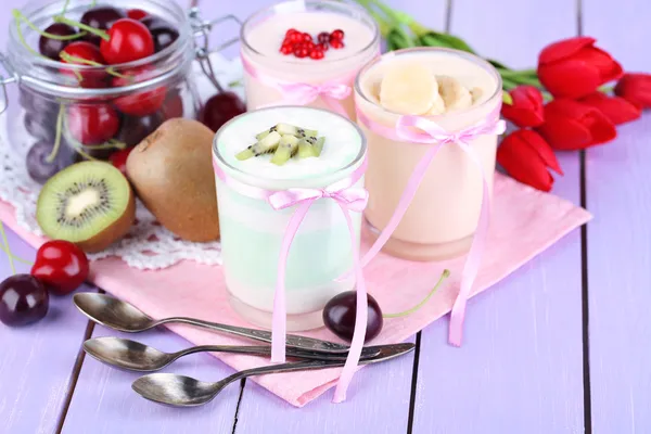Iogurte delicioso com sabores de frutas em copos e frutas frescas em fundo de madeira cor — Fotografia de Stock