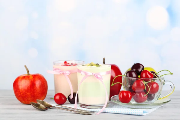 Lahodný jogurt s ovocem chutná na brýle a čerstvé ovoce na ubrousek, na barevný dřevěný stůl, na světlé pozadí — Stock fotografie