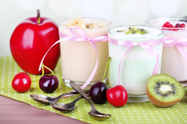 Heerlijke yoghurt met fruit smaken in glazen en vers fruit op kleur servet, op lichte achtergrond — Stockfoto