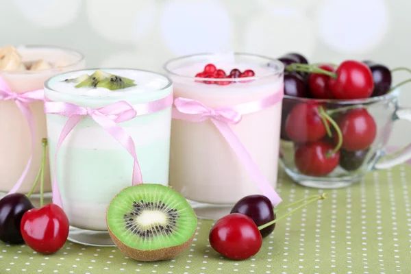 Delizioso yogurt con gusti di frutta in bicchieri e frutta fresca su tovagliolo di colore, su sfondo chiaro — Foto Stock