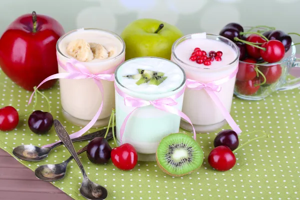 Delicioso yogur con sabores de frutas en vasos y frutas frescas sobre fondo de servilleta de color —  Fotos de Stock