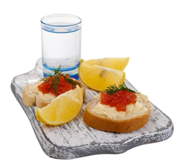 Sanduíches com caviar e vodka em tábua de madeira isolada em branco — Fotografia de Stock