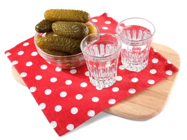 Glasses of vodka and salted cucumbers on wooden board isolated on white — Stock Photo, Image