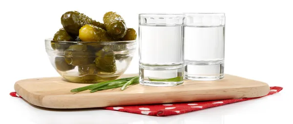 Glasses of vodka and salted cucumbers on wooden board isolated on white — Stock Photo, Image