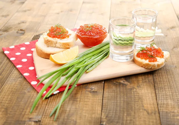 Caviar rojo en tazón y vodka sobre tabla de madera, sobre servilleta sobre fondo de madera —  Fotos de Stock