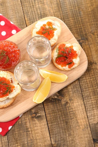 Caviar rojo en tazón y vodka sobre tabla de madera, sobre servilleta sobre fondo de madera —  Fotos de Stock