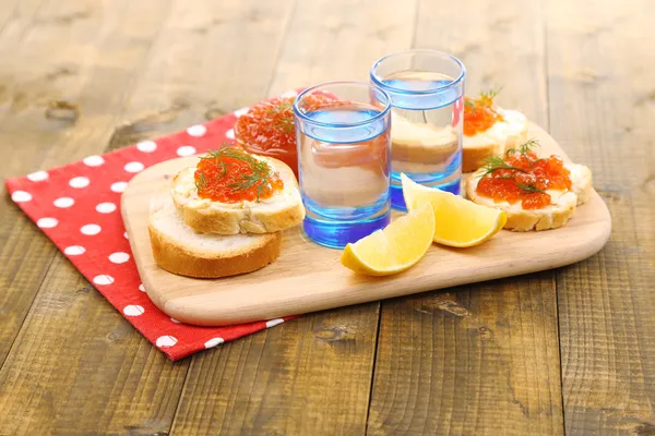 Caviar rojo en tazón y vodka sobre tabla de madera, sobre servilleta sobre fondo de madera — Foto de Stock