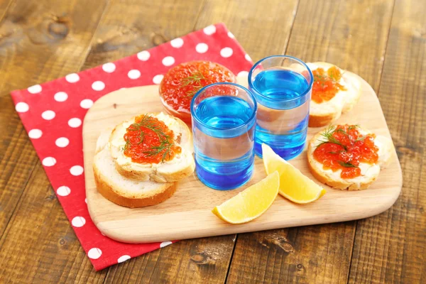 Caviar rojo en tazón y vodka sobre tabla de madera, sobre servilleta sobre fondo de madera —  Fotos de Stock
