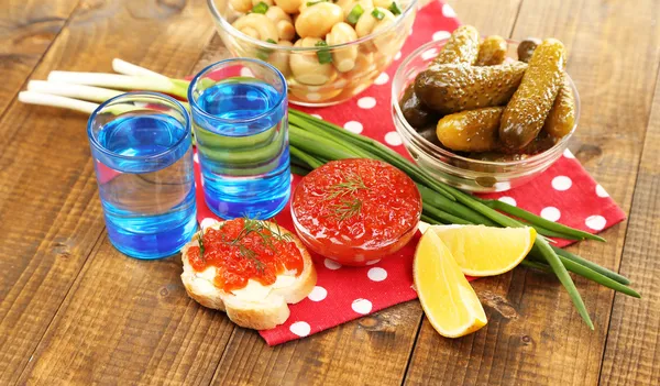 Composição com vidro de vodka e cogumelos marinados, pepinos em fundo de madeira — Fotografia de Stock