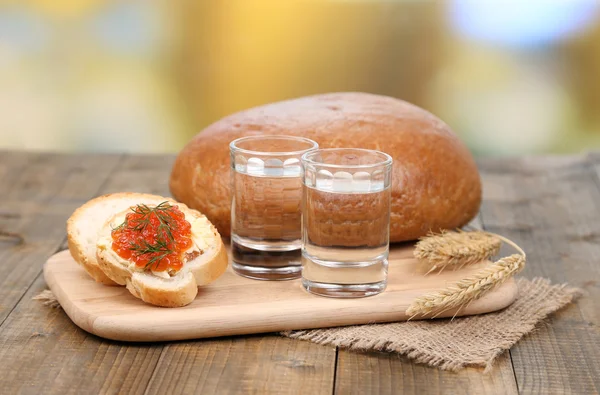 Kompozycja z kieliszków wódki chleb i kawior czerwony na drewnianym stole, na jasnym tle — Zdjęcie stockowe