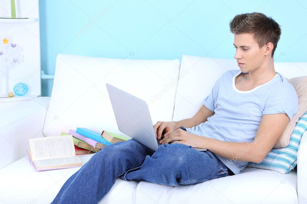 Guy sitting on sofa with laptop on blue background