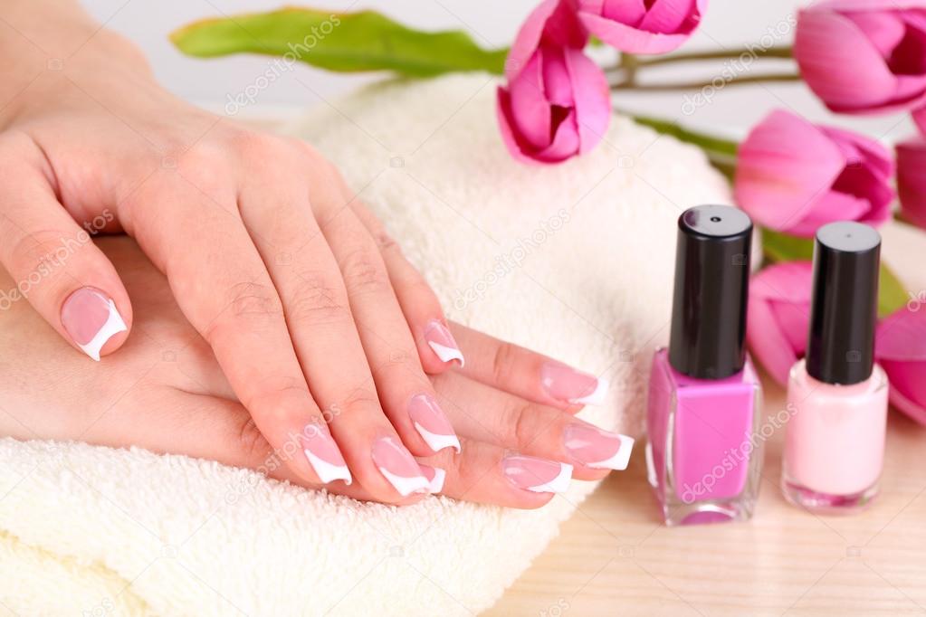 Beautiful woman hands with french manicure and flowers on table close up