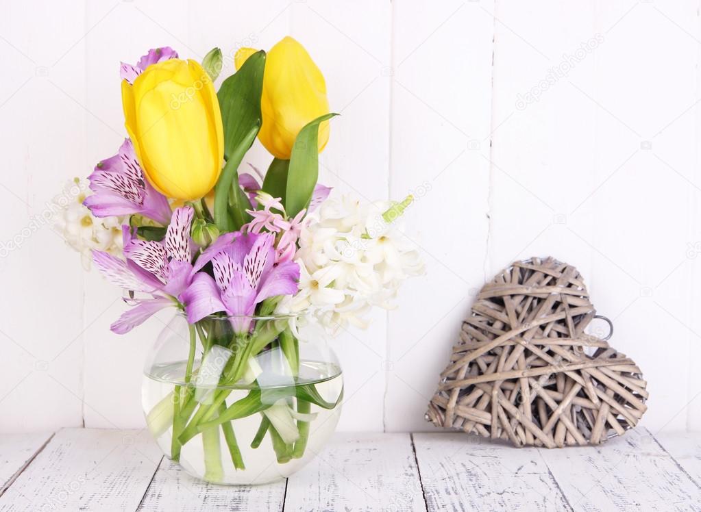 Flowers in vase with decorative heart on table on wooden background