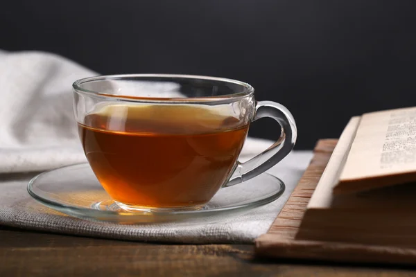 Beker van hete thee met boek op tafel op donkere achtergrond — Stockfoto