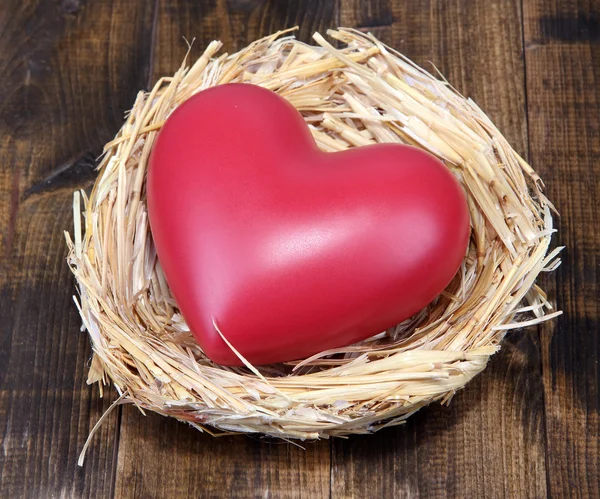 Decorative heart in nest, on wooden background — Stock Photo, Image