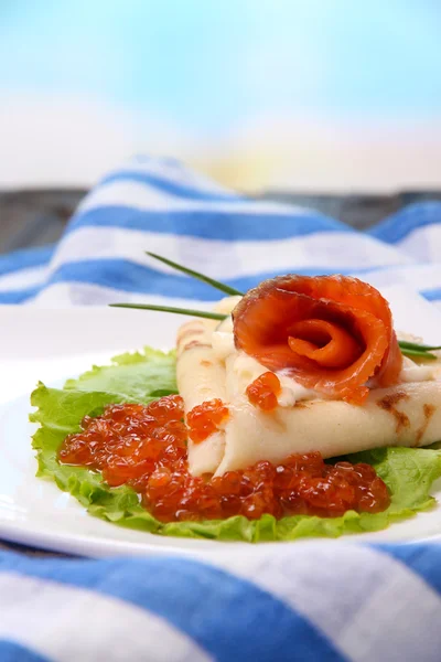 Pannenkoek met rode kaviaar, zalm en mayo, groene ui, op plaat, op kleur servet, op houten tafel, op lichte achtergrond — Stockfoto