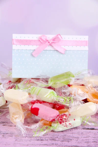 Sabrosos caramelos con tarjeta en la mesa sobre fondo brillante — Foto de Stock