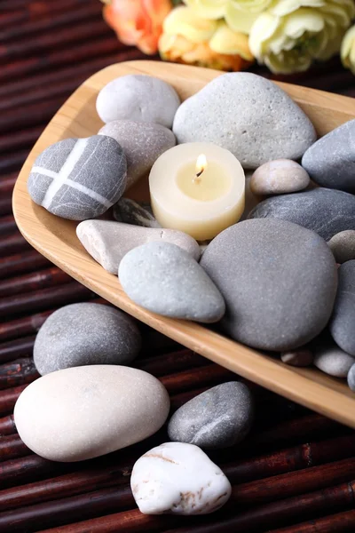 Tigela de madeira com pedras de spa e velas na mesa de madeira, no fundo flores — Fotografia de Stock