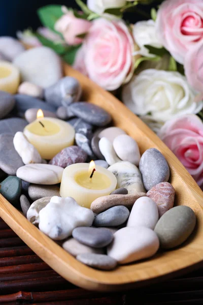Wooden bowl with spa stones and candles on wooden  table, on flowers background — Stock Photo, Image