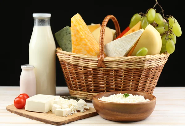 Basket with tasty dairy products on wooden table, on dark brown background — Stock Photo, Image