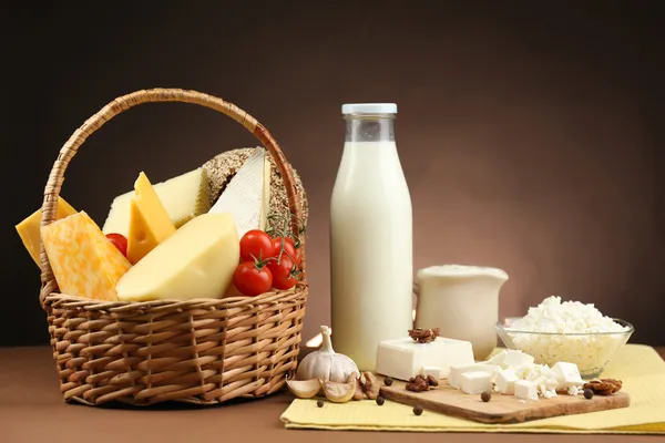 Cesta com produtos lácteos saborosos na mesa de madeira, no fundo marrom escuro — Fotografia de Stock