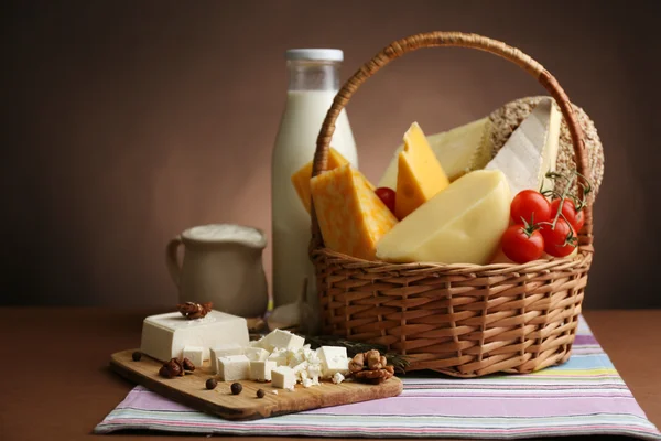 Корзина с вкусными молочными продуктами на деревянном столе, на темно-коричневом фоне — стоковое фото