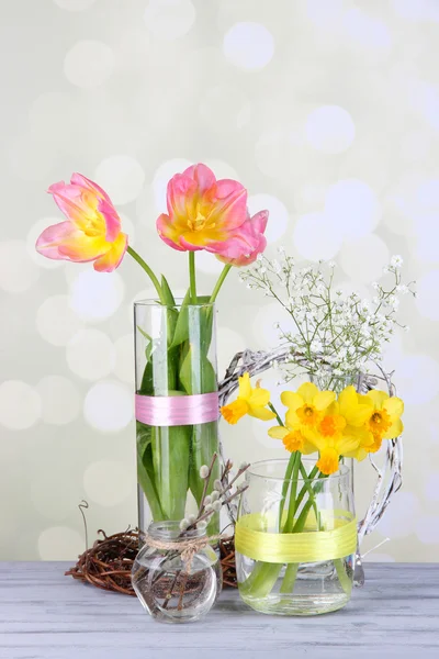 Beautiful spring flowers on old wooden table, on light background — Stock Photo, Image