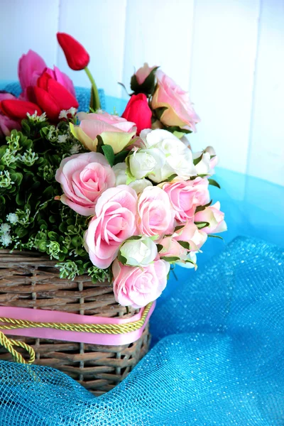 Beautiful flowers in wicker basket, on color fabric and  wooden background — Stock Photo, Image