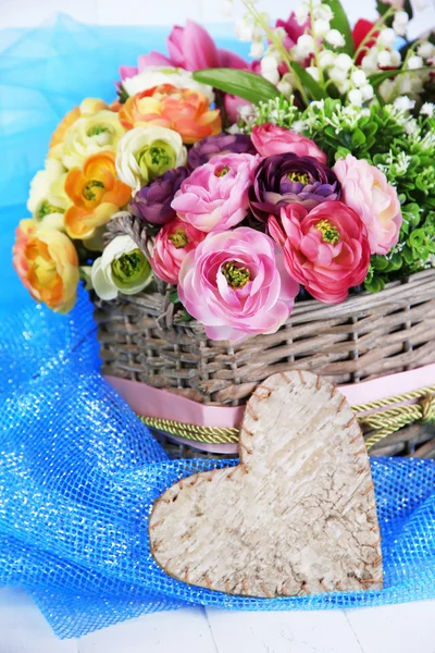 Piękne kwiaty w wiklinowym koszu, na kolor tkaniny i drewniane tła — Zdjęcie stockowe