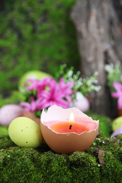 Composição conceitual da Páscoa. Vela ardente em ovo, ovos de Páscoa e flores no fundo de grama verde, close-up — Fotografia de Stock